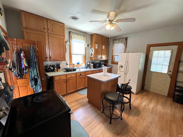 kitchen with black appliances, a kitchen island, a wealth of natural light, and light hardwood / wood-style flooring