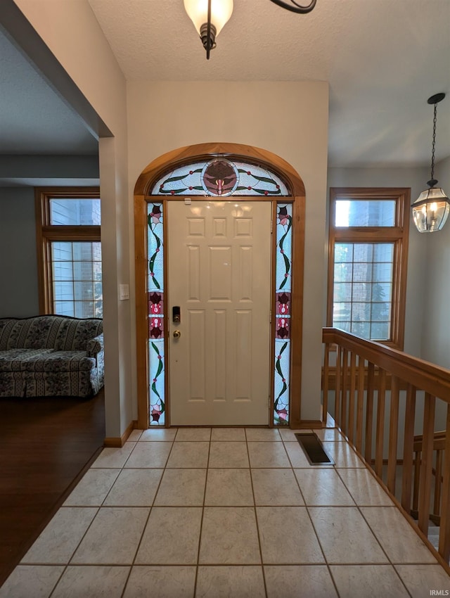 tiled entryway with a notable chandelier and a textured ceiling