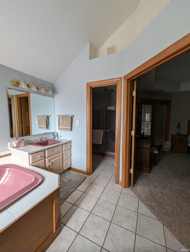 bathroom featuring vanity, vaulted ceiling, a textured ceiling, a tub to relax in, and tile patterned flooring