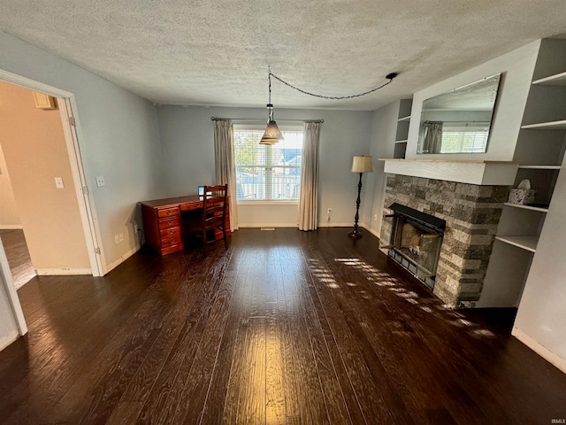 living room with a stone fireplace, a textured ceiling, dark hardwood / wood-style floors, and built in features