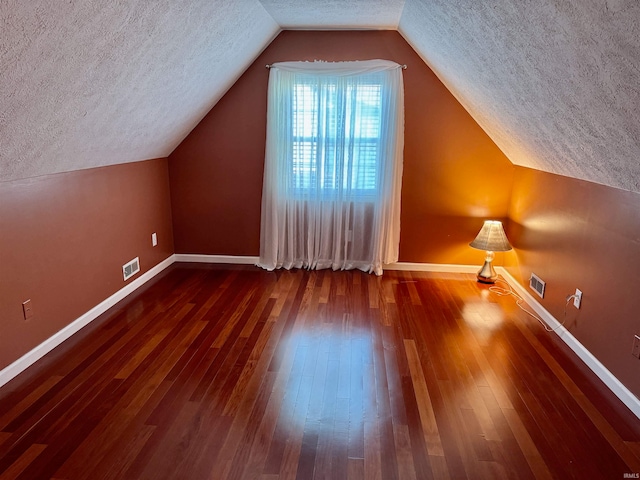 additional living space featuring a textured ceiling, lofted ceiling, and dark hardwood / wood-style flooring