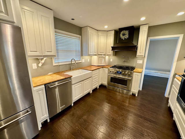 kitchen with sink, white cabinets, custom exhaust hood, appliances with stainless steel finishes, and dark hardwood / wood-style flooring