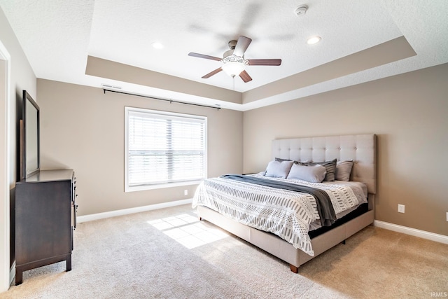 bedroom featuring ceiling fan, light colored carpet, and a tray ceiling