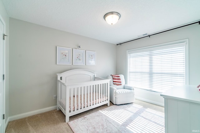 carpeted bedroom with a textured ceiling and a nursery area