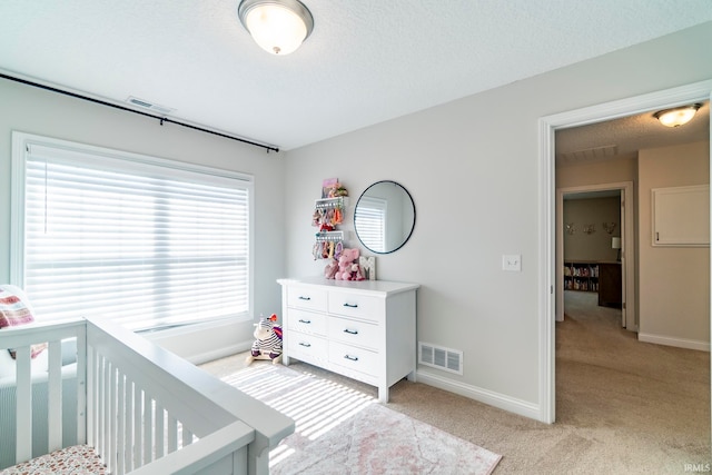 bedroom featuring a textured ceiling, light carpet, and a nursery area