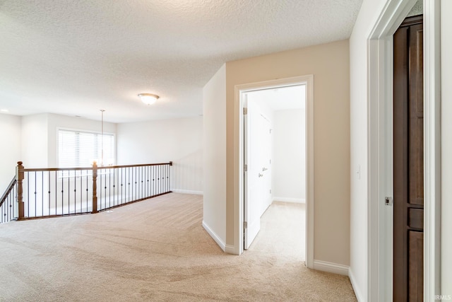 hall featuring a textured ceiling, an inviting chandelier, and light carpet