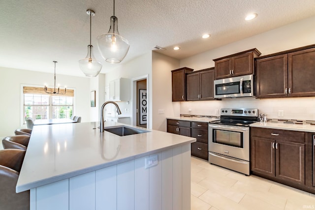 kitchen featuring pendant lighting, a textured ceiling, sink, an island with sink, and appliances with stainless steel finishes