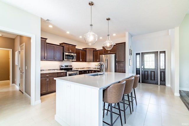 kitchen with a breakfast bar area, an island with sink, sink, hanging light fixtures, and stainless steel appliances