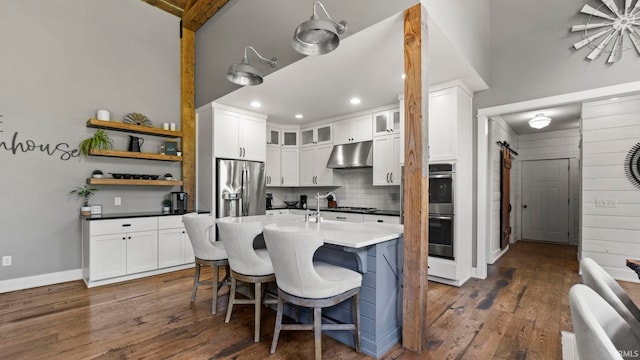 kitchen with dark wood-type flooring, white cabinetry, a barn door, stainless steel appliances, and backsplash