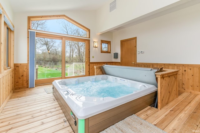 interior space with light hardwood / wood-style flooring, wooden walls, vaulted ceiling, and a jacuzzi