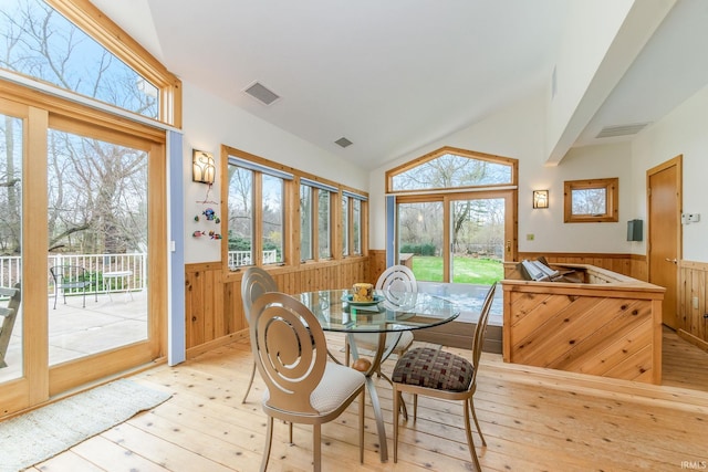 dining space featuring light hardwood / wood-style floors, wood walls, and vaulted ceiling