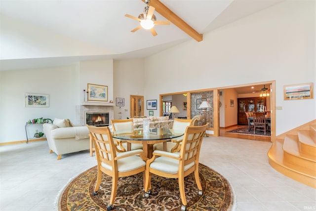 dining space with light tile patterned floors, a fireplace, ceiling fan, and beamed ceiling