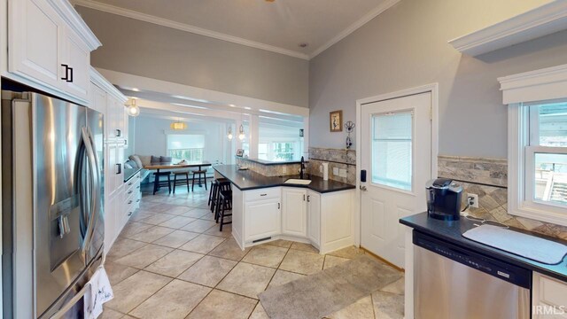 kitchen with appliances with stainless steel finishes, light tile patterned flooring, white cabinets, backsplash, and ornamental molding