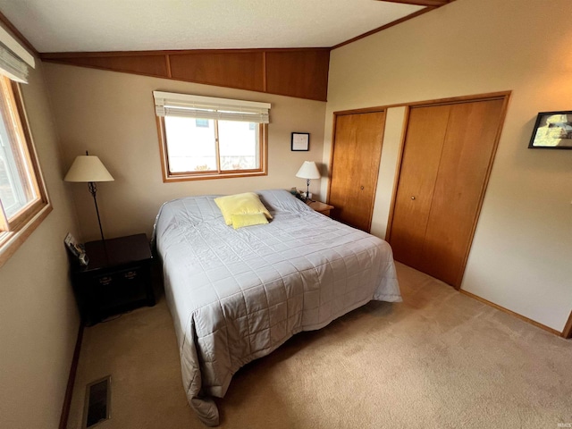 carpeted bedroom featuring multiple closets and vaulted ceiling