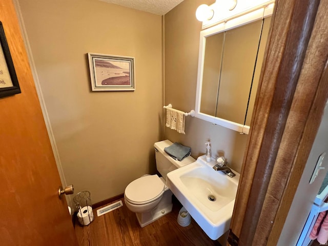 bathroom with wood-type flooring, a textured ceiling, sink, and toilet