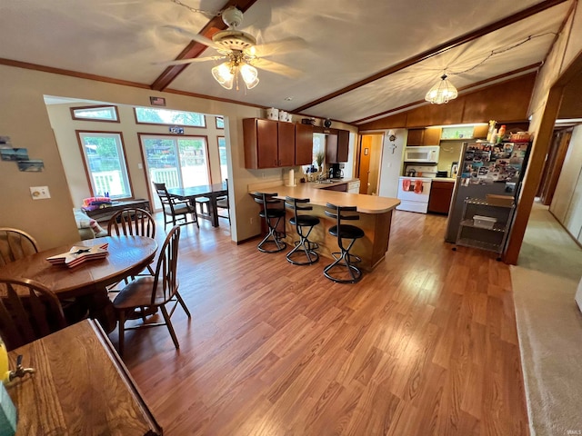 kitchen featuring ceiling fan, kitchen peninsula, white appliances, a kitchen bar, and vaulted ceiling