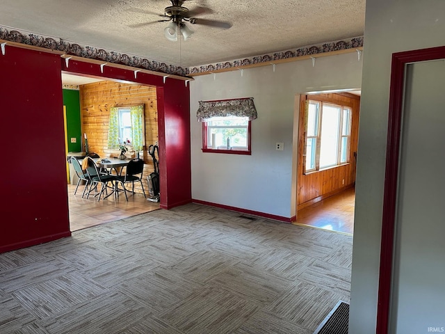 unfurnished room with ceiling fan, light colored carpet, a textured ceiling, and wooden walls