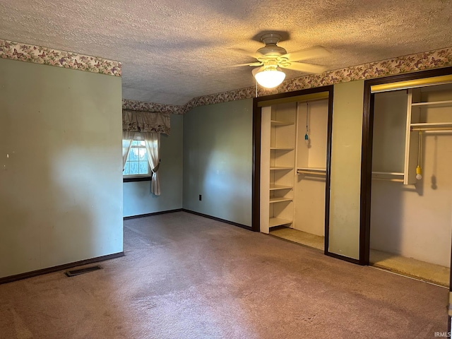 unfurnished bedroom featuring ceiling fan, a textured ceiling, two closets, and carpet flooring