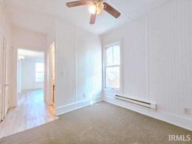 spare room featuring carpet floors, ceiling fan, and a baseboard heating unit