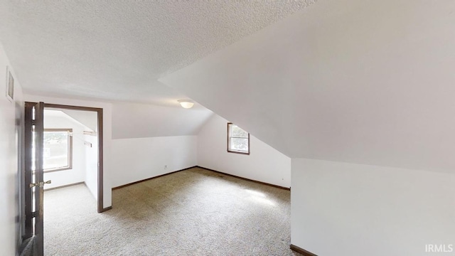 additional living space featuring lofted ceiling, a textured ceiling, and light colored carpet