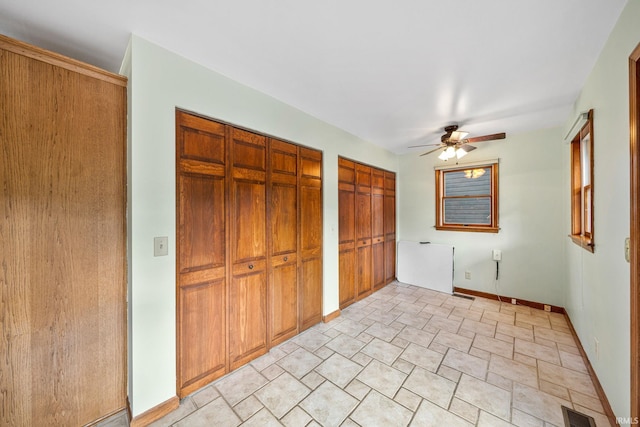 unfurnished bedroom with ceiling fan and two closets