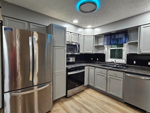 kitchen featuring appliances with stainless steel finishes, gray cabinetry, a textured ceiling, light wood-type flooring, and sink