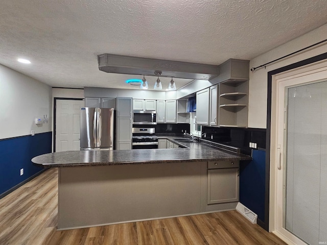 kitchen with light wood-type flooring, kitchen peninsula, sink, and stainless steel appliances