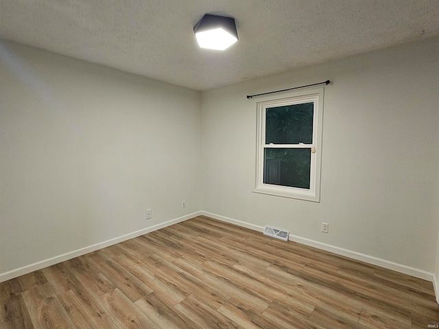 unfurnished room with light wood-type flooring and a textured ceiling