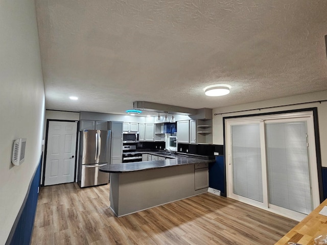 kitchen featuring light hardwood / wood-style floors, a textured ceiling, kitchen peninsula, and stainless steel appliances