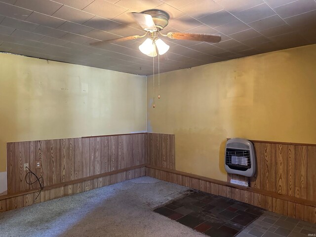 carpeted empty room featuring heating unit, ceiling fan, and wooden walls