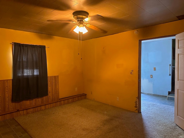 empty room with carpet, ceiling fan, and wood walls