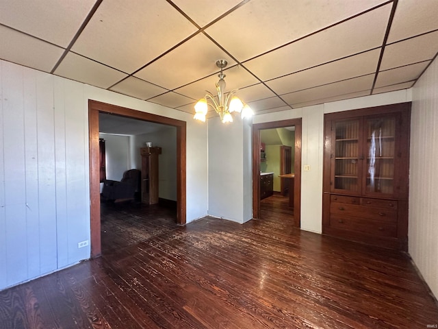 empty room featuring a drop ceiling, wood walls, dark hardwood / wood-style floors, and a notable chandelier