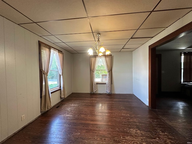 empty room featuring an inviting chandelier, a drop ceiling, and dark hardwood / wood-style flooring