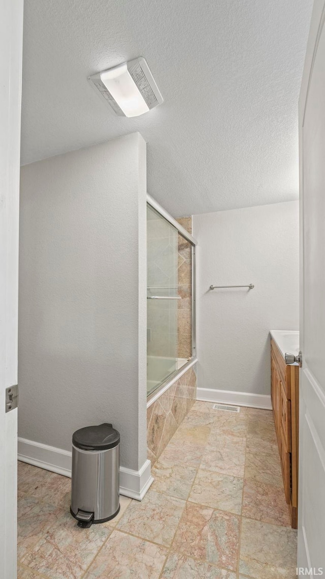 bathroom with a textured ceiling, enclosed tub / shower combo, and vanity