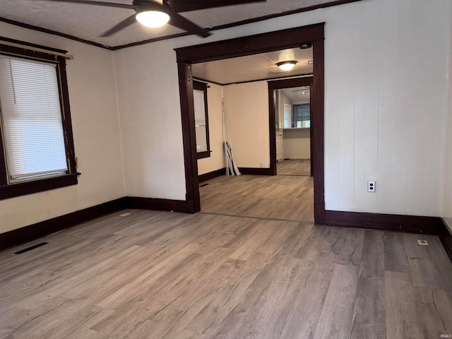 empty room featuring ceiling fan, a textured ceiling, light wood-type flooring, and ornamental molding