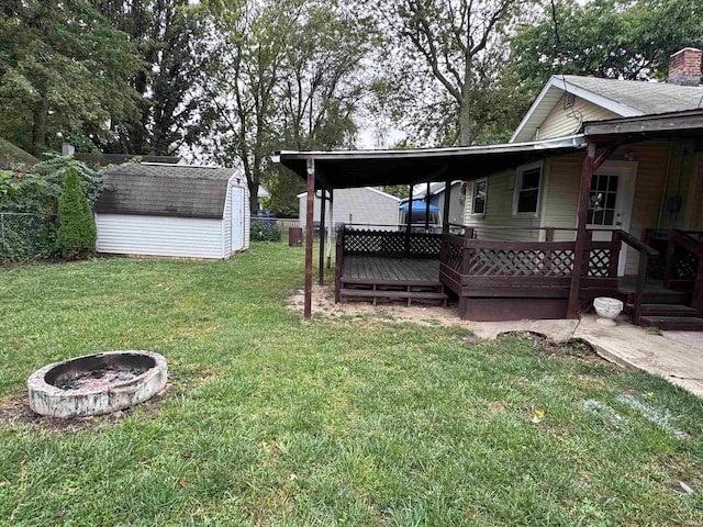 view of yard featuring a wooden deck, a storage shed, and an outdoor fire pit