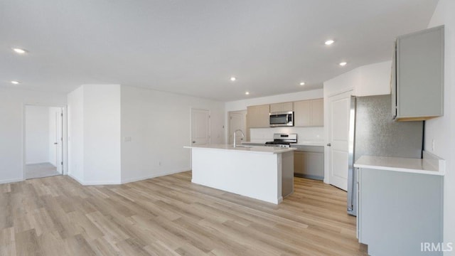 kitchen featuring appliances with stainless steel finishes, gray cabinetry, sink, a center island with sink, and light hardwood / wood-style floors