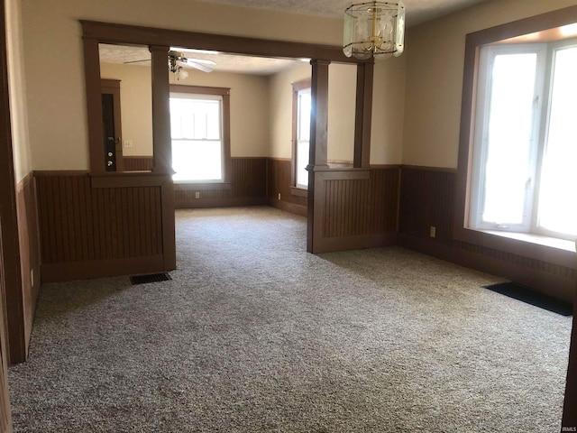 carpeted spare room featuring ceiling fan with notable chandelier and wood walls