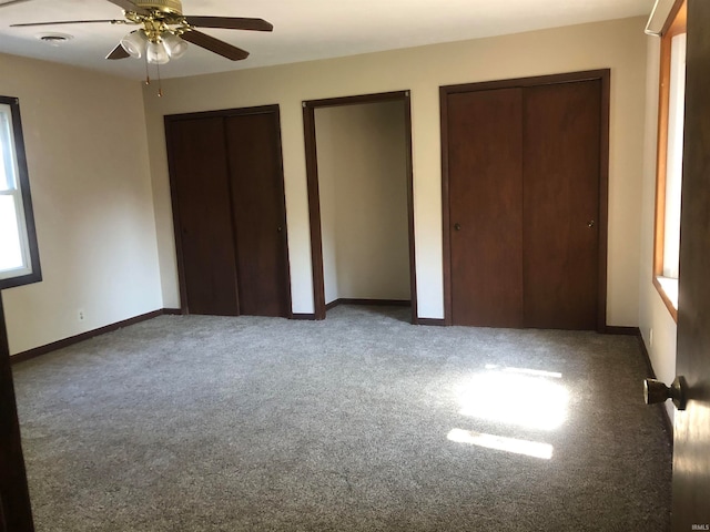 unfurnished bedroom featuring ceiling fan, carpet floors, and two closets