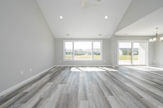 unfurnished living room with ceiling fan with notable chandelier, light hardwood / wood-style flooring, and high vaulted ceiling