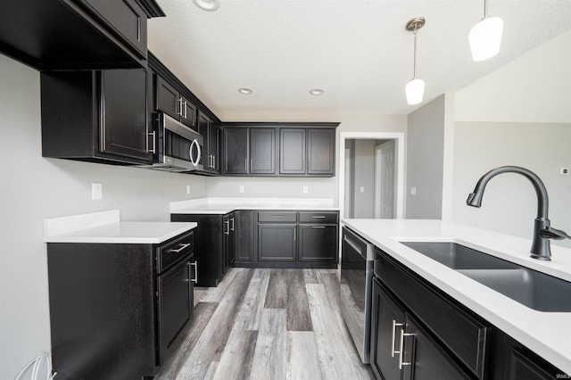 kitchen with a textured ceiling, sink, hanging light fixtures, light hardwood / wood-style flooring, and stainless steel appliances