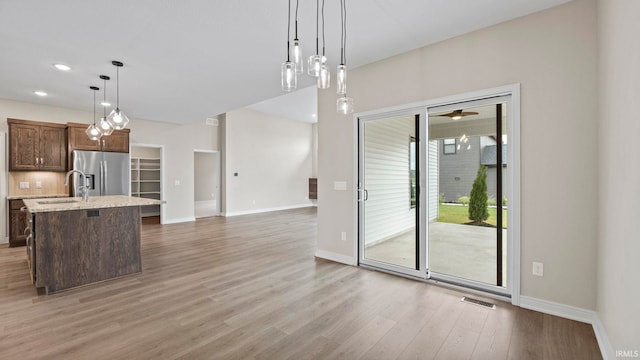 kitchen with hardwood / wood-style flooring, a center island with sink, hanging light fixtures, and stainless steel refrigerator with ice dispenser