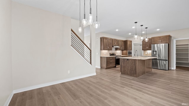 kitchen with light wood-type flooring, sink, a center island with sink, appliances with stainless steel finishes, and decorative light fixtures