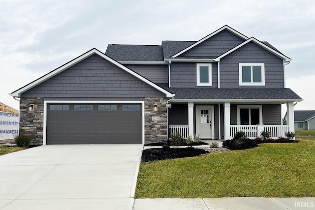 craftsman inspired home with driveway, covered porch, stone siding, a front yard, and a garage