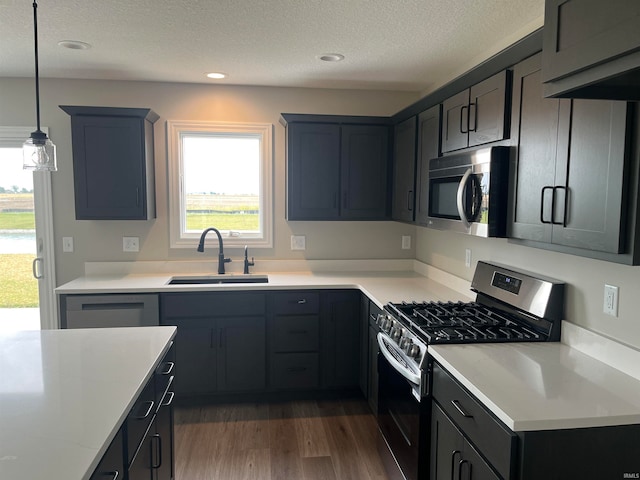 kitchen with a textured ceiling, appliances with stainless steel finishes, decorative light fixtures, dark hardwood / wood-style flooring, and sink