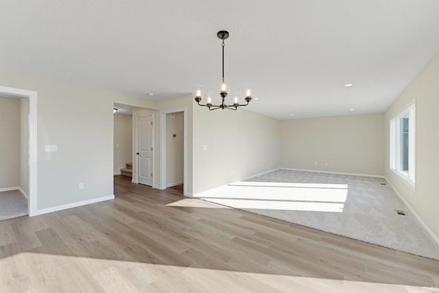 spare room featuring baseboards, an inviting chandelier, and light wood-type flooring
