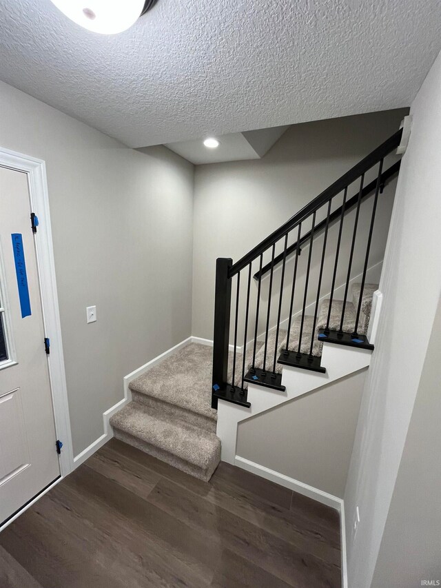 staircase featuring a textured ceiling and hardwood / wood-style flooring