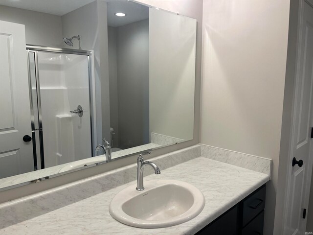 bathroom with a shower with shower door, vanity, and toilet