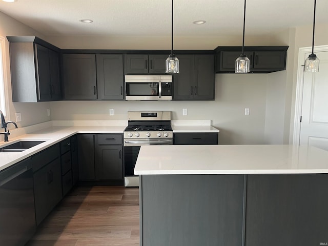 kitchen with appliances with stainless steel finishes, dark hardwood / wood-style floors, hanging light fixtures, a kitchen island, and sink