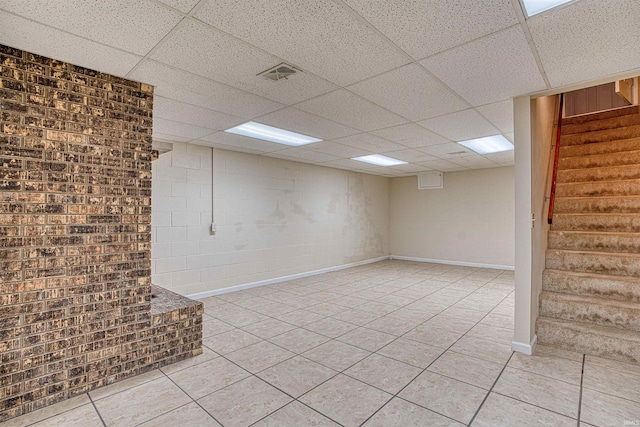 basement with brick wall, a drop ceiling, and light tile patterned floors